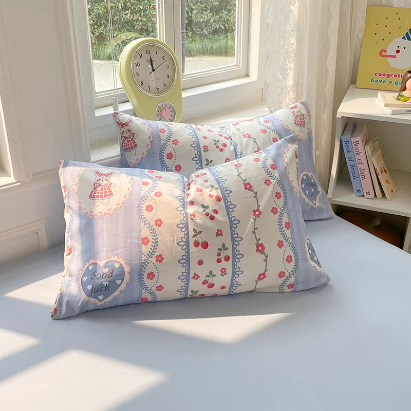 A light blue duvet cover set with patterned pillowcases and a yellow alarm clock on a white bed.