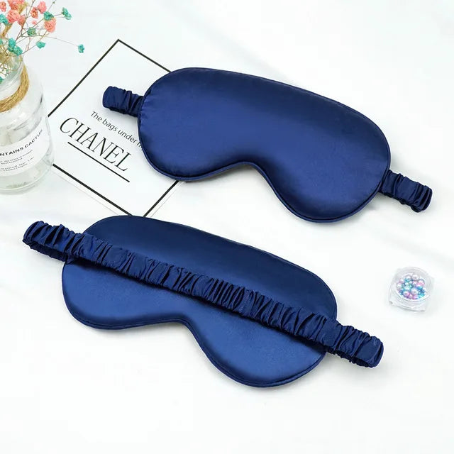A dark blue silk sleep mask with ruffled edges is displayed next to a Chanel box.