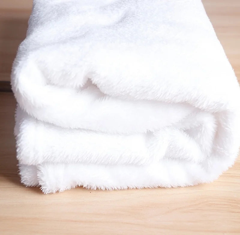 A stack of white, fluffy flannel throw blankets folded neatly on a wooden surface.