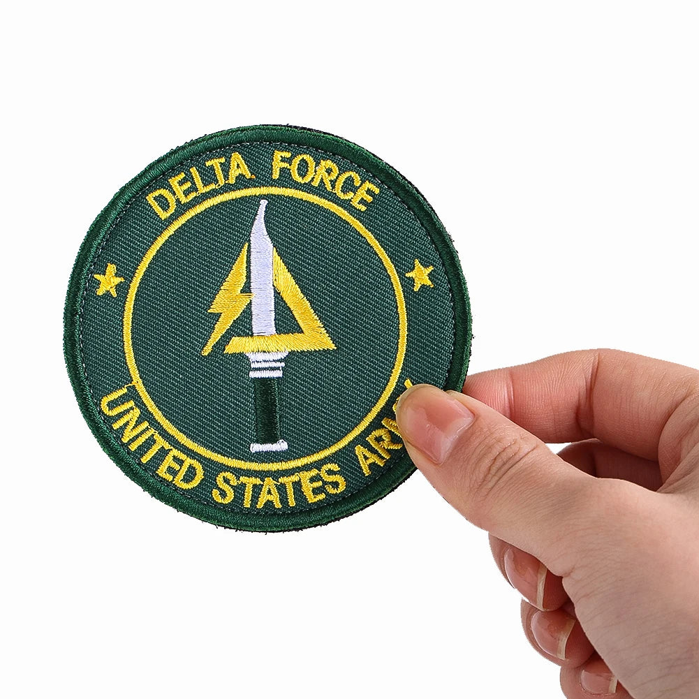 A round olive green embroidery patch with yellow text and a stylized lightning bolt sword design.