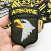 A close-up of an embroidered Airborne patch featuring a white eagle head on a dark olive green background.