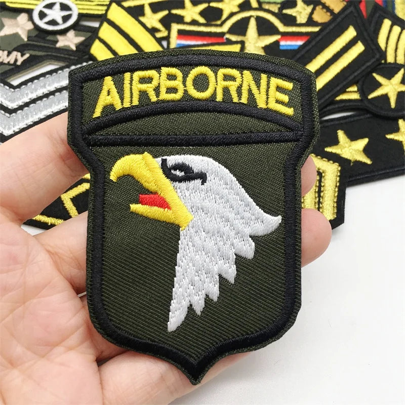 A close-up of an embroidered Airborne patch featuring a white eagle head on a dark olive green background.
