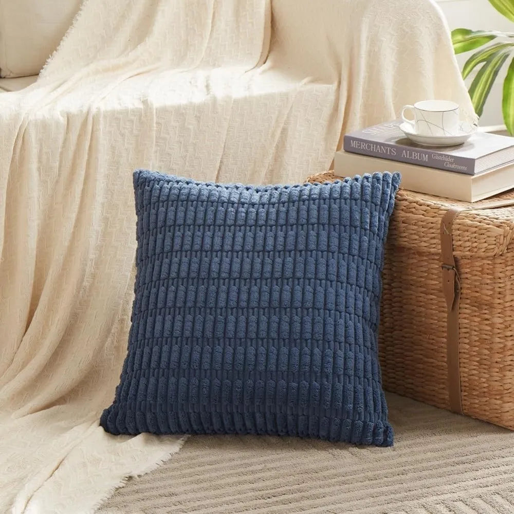 A dark blue knitted throw pillow resting on a light beige blanket next to a woven basket.