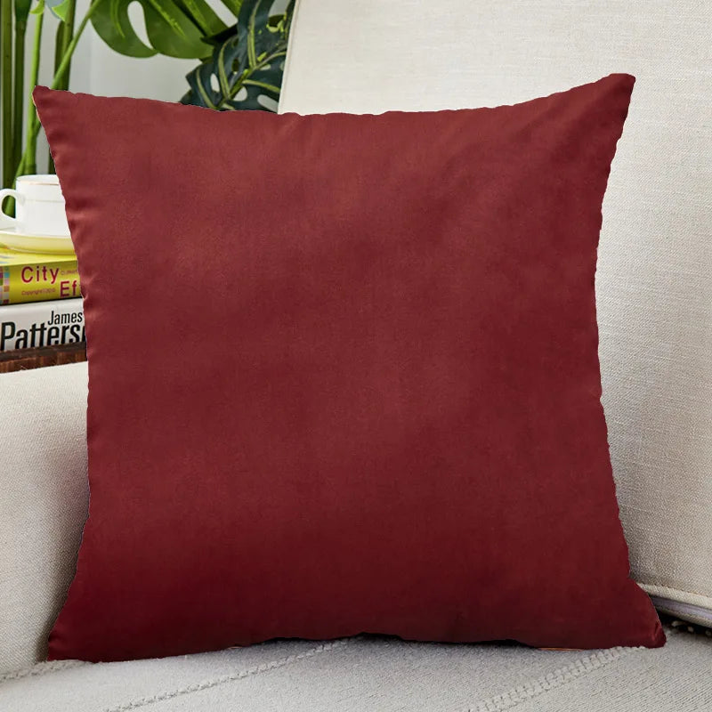 A square, deep burgundy velvet cushion cover resting on a light-colored sofa.