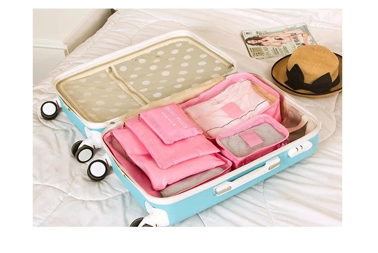 A light blue travel organizer storage set with a lid and multiple pink fabric pouches is displayed on a white bed.