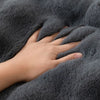 A hand is gently touching a dark gray plush velvet sofa cover with a soft texture.