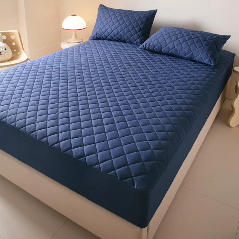 A blue quilted mattress protector is shown on a bed, featuring a diamond pattern.