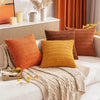 A collection of textured, woven throw pillows in shades of orange, mustard yellow, and terracotta on a light sofa.