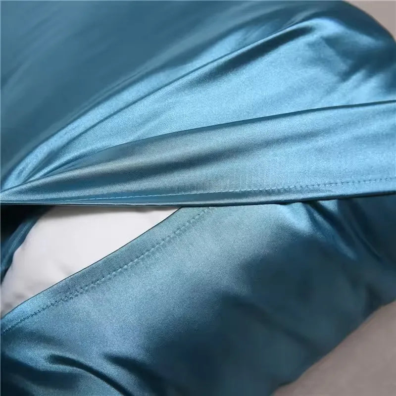A close-up of a teal silky satin pillowcase draped and folded.