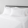 A set of four white microfiber flat fitted sheets on a bed with a silver headboard.