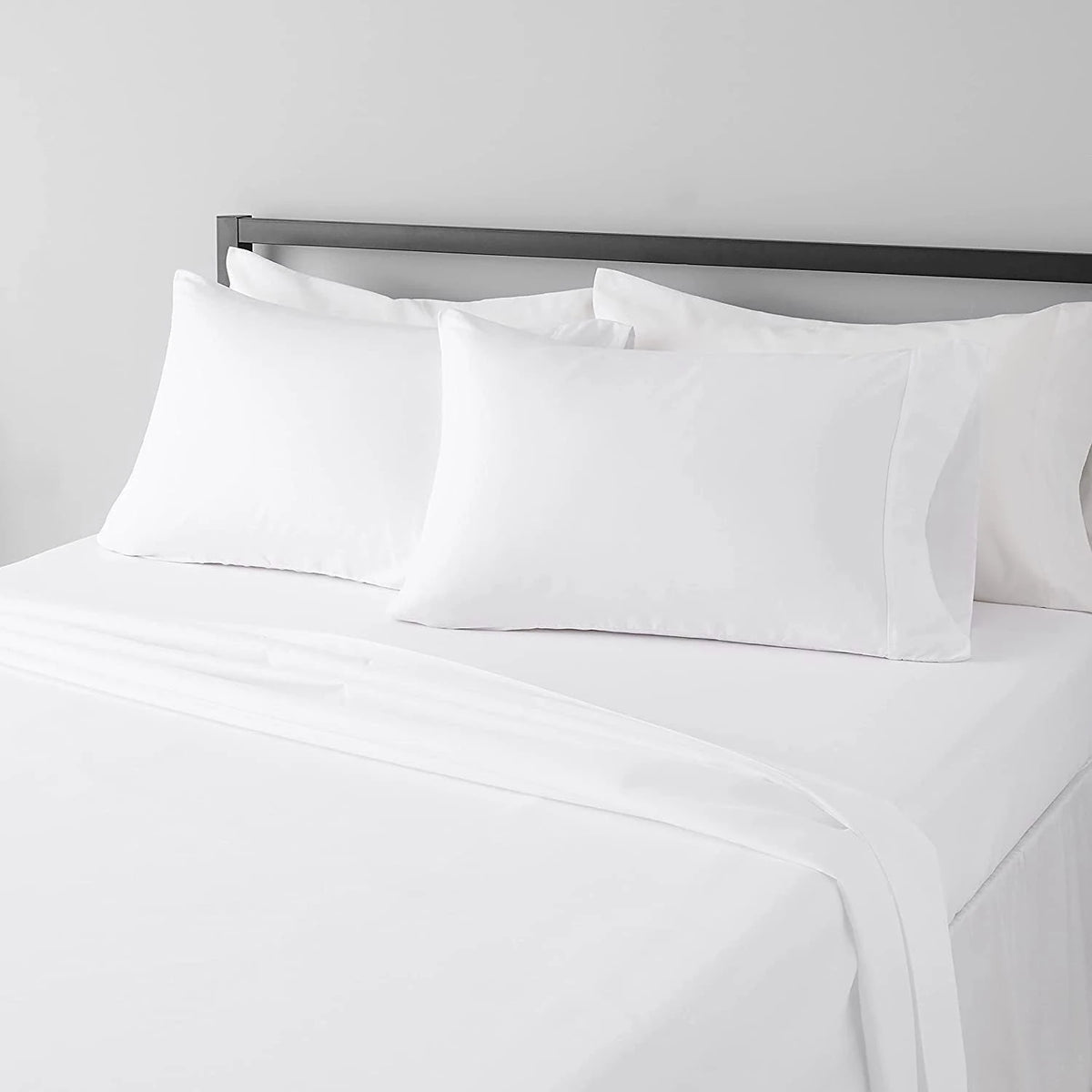 A set of four white microfiber flat fitted sheets on a bed with a silver headboard.