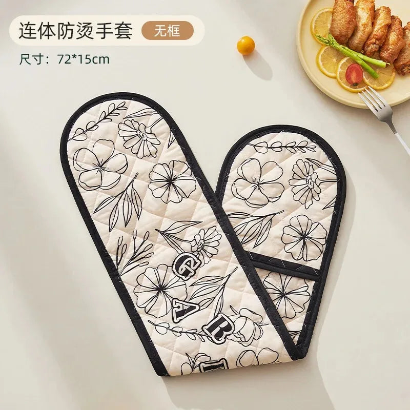 A pair of floral patterned heat-resistant oven mitts with a black trim are displayed on a white surface.