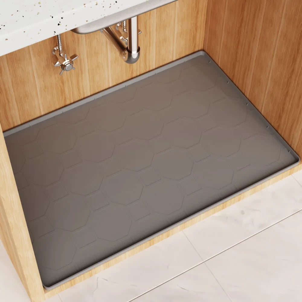 A gray silicone mat liner is placed inside a wooden under sink cabinet.