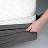 A hand is folding a gray box spring protector cover over a white mattress.