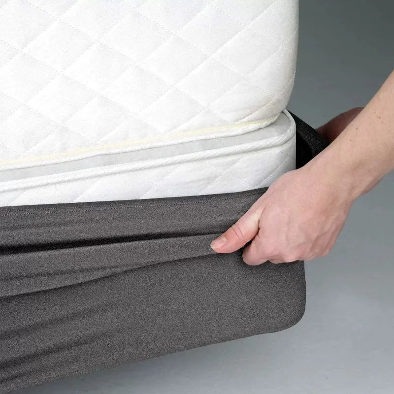 A hand is folding a gray box spring protector cover over a white mattress.