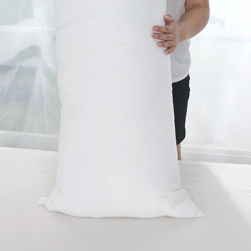 A person is holding a large white extra-long body pillow for full-body support.