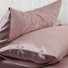 A stack of smooth, dusty rose colored luxury mulberry silk pillow covers.
