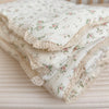 A stack of white muslin blankets with a floral print are folded on a light pink surface.