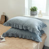 A set of two soft plaid washed cotton pillowcases with ruffled edges resting on a light brown surface.