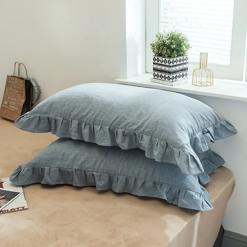 A set of two soft plaid washed cotton pillowcases with ruffled edges resting on a light brown surface.