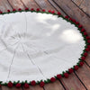 A cream knitted throw blanket with a floral pattern and a red border resting on a wooden surface.