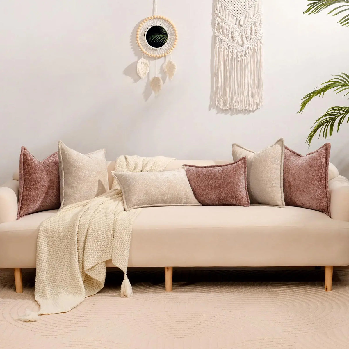 A beige sofa decorated with various textured throw pillows and a cream knitted blanket against a white wall.