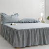 A plaid cotton bed skirt cover in blue and white checks draped over a bed.