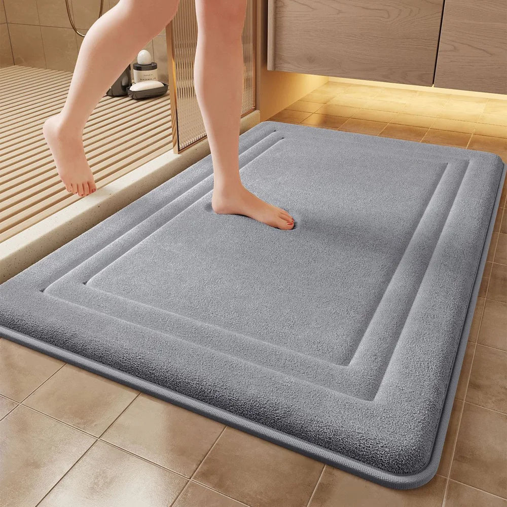 A gray ultra soft memory foam bathroom mat placed on a tiled floor next to a wooden cabinet.