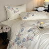 White embroidered orchid duvet cover set with lace trim displayed on a bed.