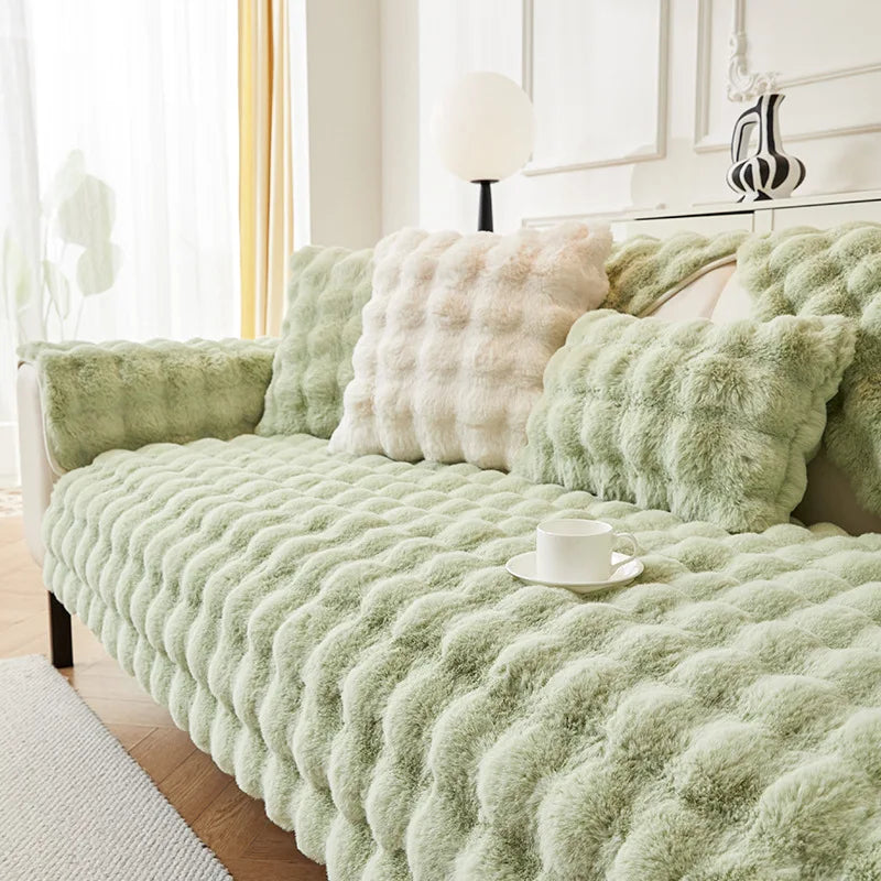 A light green plush rabbit fur sofa cushion cover with a cream accent pillow on a white sofa.