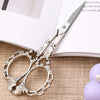A pair of silver crafting scissors resting on a light-colored notebook or paper.