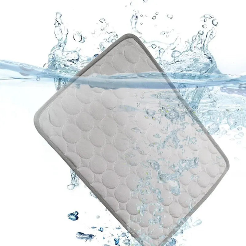 A gray cooling ice mat for pets is shown partially submerged in water with splashing droplets.
