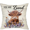 A decorative pillow cover featuring an illustration of a brown Highland cow surrounded by purple and yellow wildflowers.