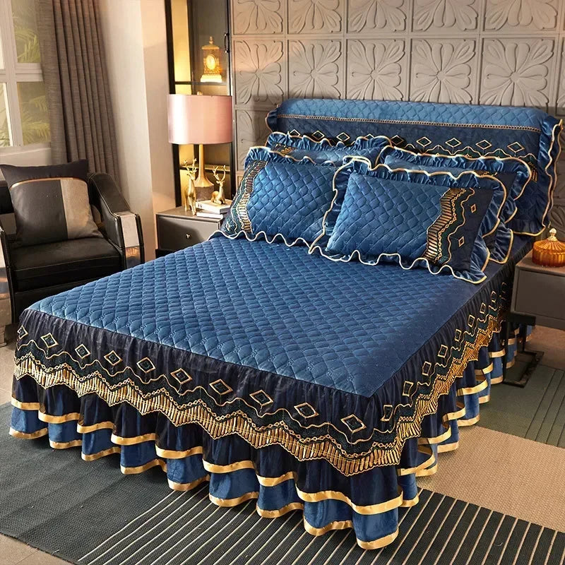 A deep blue quilted velvet bed skirt with gold trim and decorative tassels is displayed on a bed.