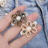 A hand holds a gold-toned metal flower clip with a pearl center against a denim fabric background.
