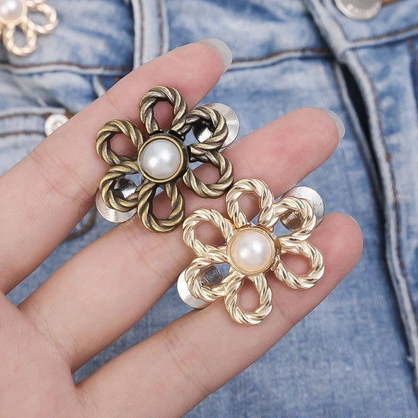 A hand holds a gold-toned metal flower clip with a pearl center against a denim fabric background.