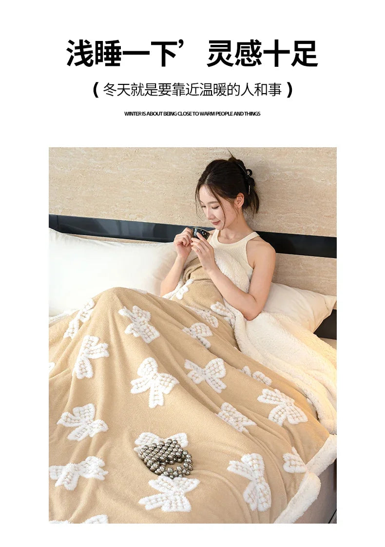 A woman is relaxing in bed under a thick beige jacquard lambswool blanket with white floral patterns.