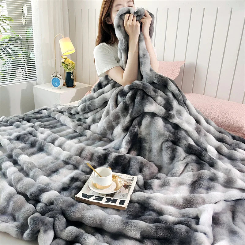 A gray plush rabbit fur throw blanket draped over a person, with a cup of tea resting on the fabric.
