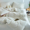 A white cotton yarn-dyed duvet cover with several pillows and an open book on a bed.