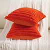 An orange textured cushion cover with vertical pleats resting on a white knitted fabric.