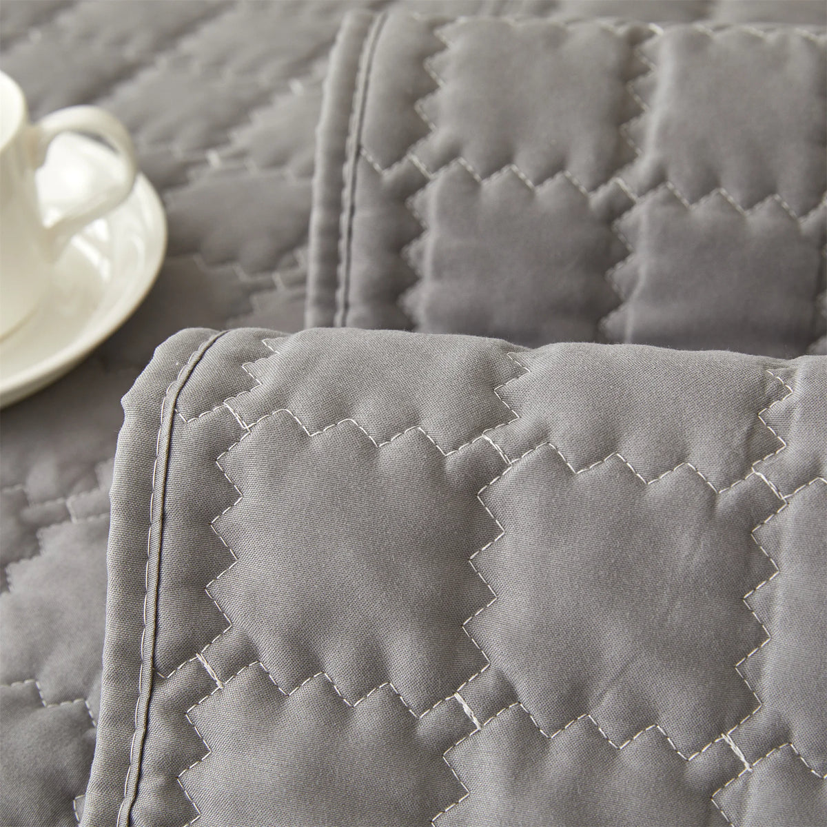 A close-up of a gray quilted anti-slip sofa cover with a plush texture lying on a surface.