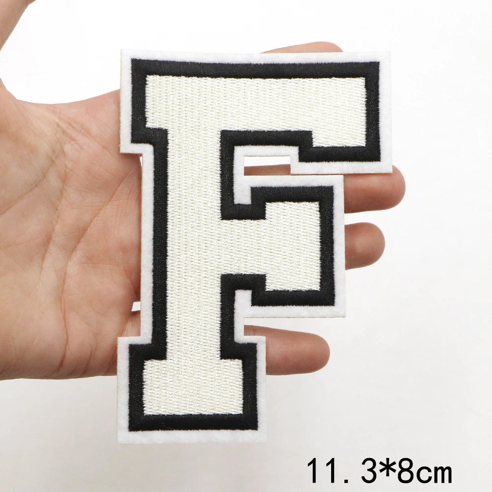 A hand holds a black and cream letter F patch for clothing decoration.