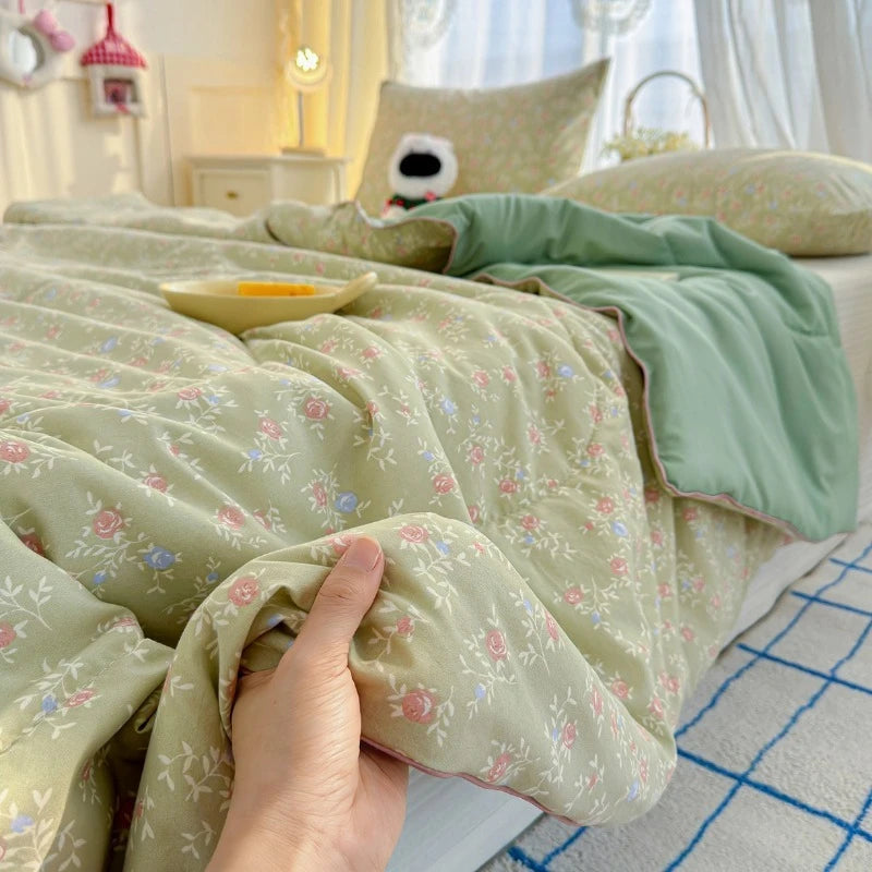 A hand is touching a light green floral quilt with pink accents on a bed, featuring soft natural lighting.