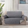 A gray slip-on protective sofa cover for a two-seater armchair with light beige trim.