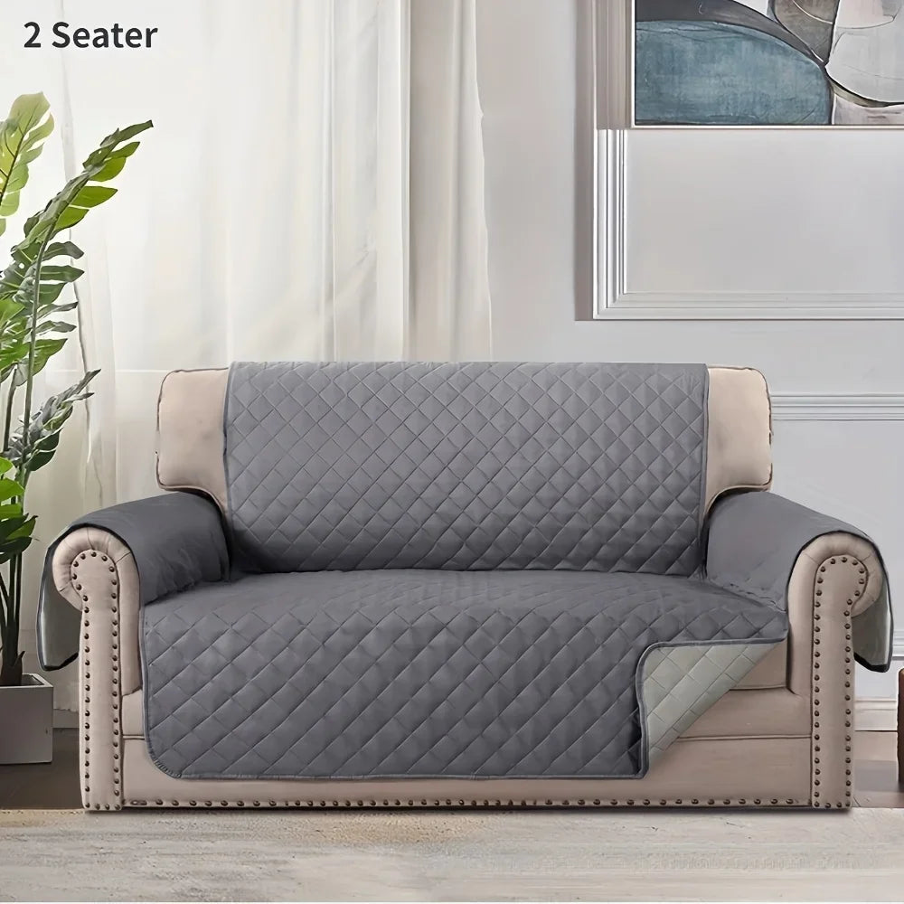 A gray slip-on protective sofa cover for a two-seater armchair with light beige trim.