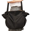 A black foldable tote bag is shown being carried by a person wearing a checkered shirt.