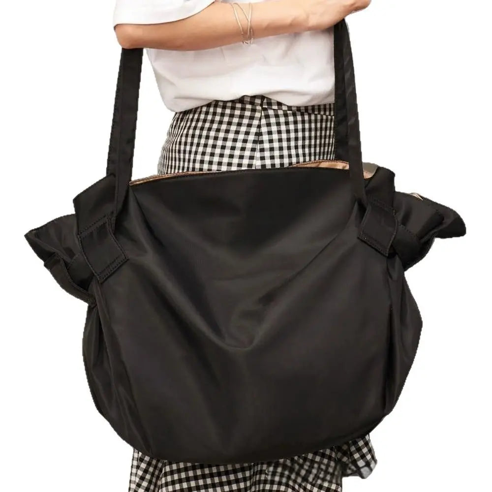A black foldable tote bag is shown being carried by a person wearing a checkered shirt.