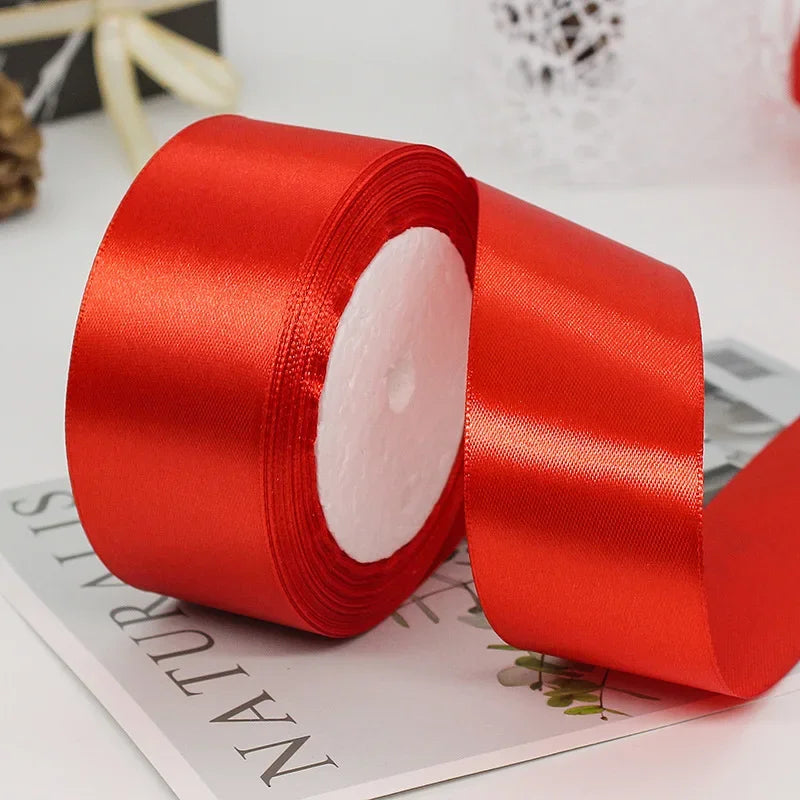 A roll of bright red satin ribbon with white filling, lying on a white surface.