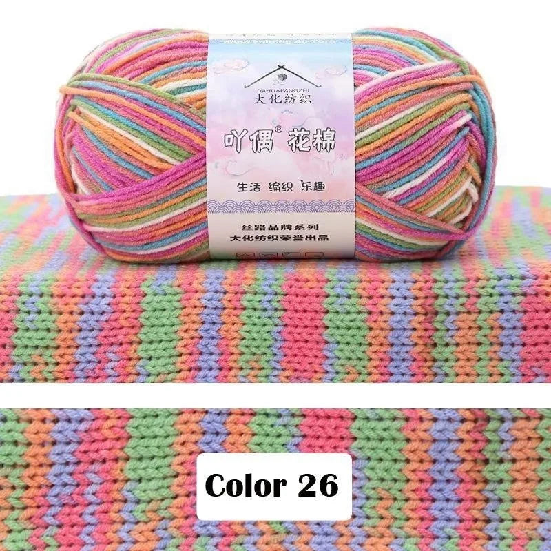 A skein of multi-colored 4-ply cotton knit yarn with a gradient pattern displayed against a textured green background.