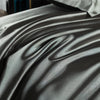 A close-up of a smooth, gray satin fitted sheet draped and folded on a bed.